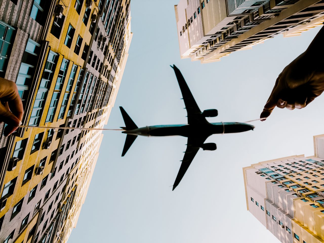 The Art of Drawing Readers In: Your attractive post title goes here A toy airplane held with string appears flying between high-rise buildings against the sky.