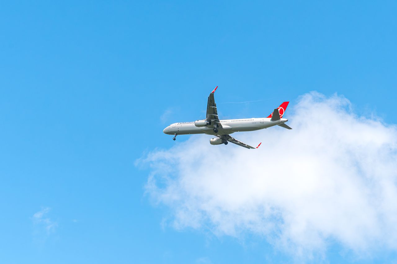 Commercial airplane flying high in the sky with a clear, bright blue backdrop and white clouds.