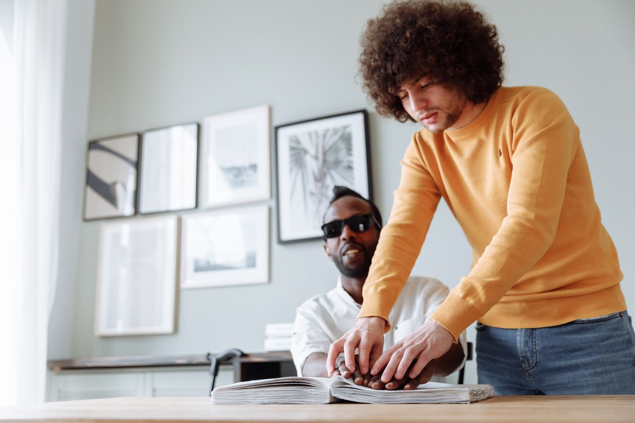 Mastering the First Impression: Your intriguing post title goes here Two men engaged in Braille reading, promoting assistive technology and independence.